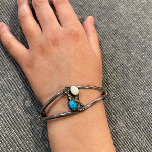 Könnte beinhalten: Ein silbernes Armband mit einem Design aus Türkis und weißem Stein. Das Armband wird am Handgelenk einer Person getragen.