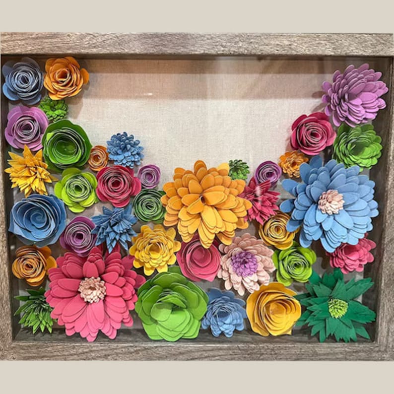 May include: A framed shadow box art piece featuring colourful paper flowers in shades of blue, green, pink, yellow, and orange. The flowers are arranged in a cascading pattern and are set against a neutral linen background.