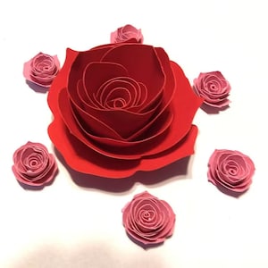 May include: A large red paper rose with multiple layers of petals surrounded by smaller pink paper roses.