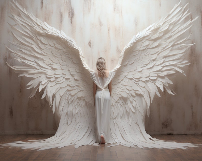 Puede incluir: Una mujer con un vestido blanco se para frente a una pared con grandes alas de &aacute;ngel de papel blanco detr&aacute;s de ella.