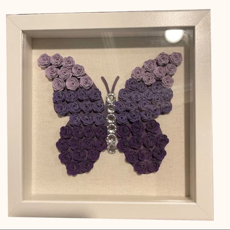 May include: A framed purple butterfly made of paper roses with a rhinestone embellishment in the centre.