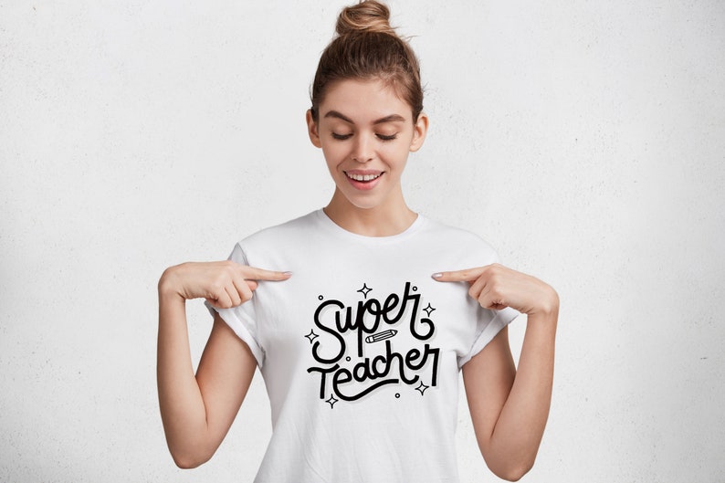 Op de afbeelding: Wit T-shirt met zwarte tekst die "Super Teacher" zegt met een potloodgrafiek.