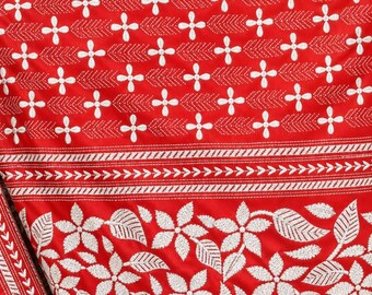 May include: A vibrant red fabric featuring white embroidered patterns. The upper section displays a repeating grid of small four-petaled flowers and chevron lines, while the lower section showcases a dense floral and leaf motif.