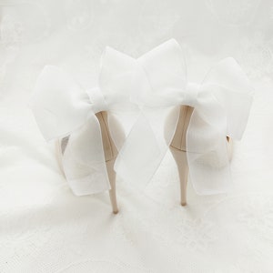 May include: Pair of ivory high-heeled shoes with large white tulle bows on the back.