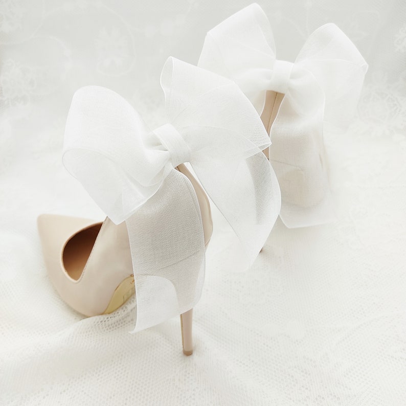 May include: A pair of nude high-heeled shoes with large white tulle bows on the back.
