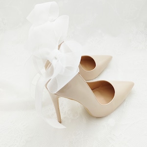 May include: A pair of nude-colored high-heeled shoes with a white satin bow on the back.