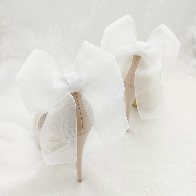 May include: A pair of nude high-heeled shoes with large white tulle bows on the back.