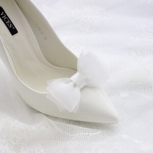 May include: White satin high heel shoe with a white tulle bow on the toe. The shoe has the brand name "VICES" and the size "EU38 41 38" written on the inside.