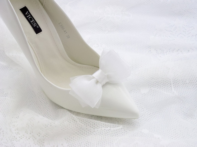 May include: White satin high heel shoe with a white tulle bow on the toe. The shoe has the brand name "VICES" and the size "EU38 41 38" written on the inside.