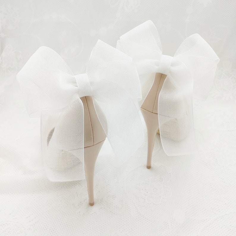 May include: A pair of nude high-heeled shoes with large white tulle bows tied around the ankles.