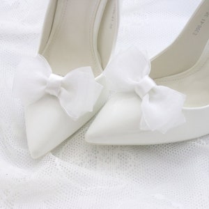 May include: Two white satin pumps with white satin bows on the toes. The shoes have a pointed toe and a high heel.