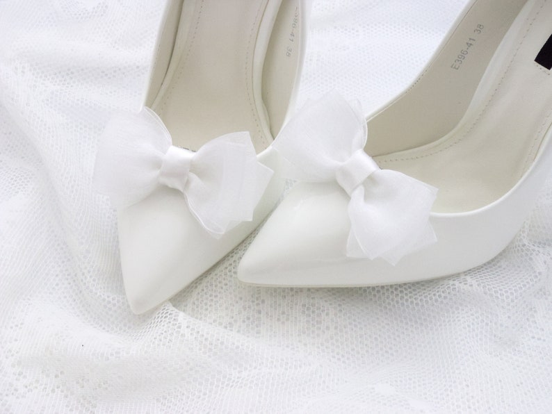 May include: Two white satin pumps with white satin bows on the toes. The shoes have a pointed toe and a high heel.