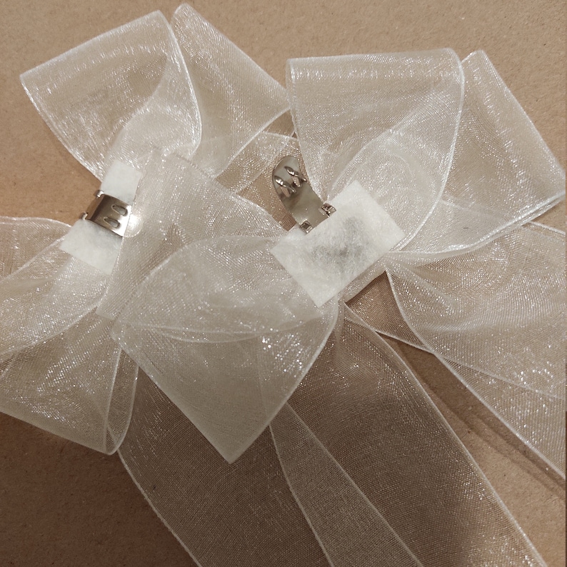May include: Two white sheer ribbon bows with silver clips. The bows are tied with a simple knot and have a shimmery finish.
