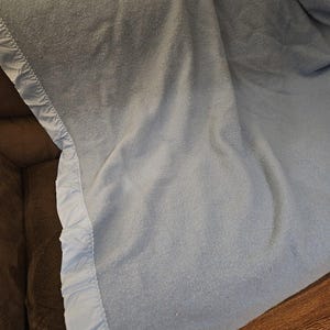 May include: A light blue blanket with a ruffled edge. The blanket is folded and draped over a brown couch.
