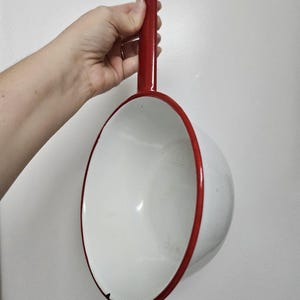 Peut inclure: Pichet en émail blanc avec un bord et une poignée rouges. La poignée a une boucle en haut.