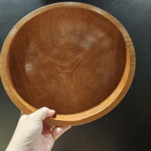 Könnte beinhalten: Eine große, runde Holzschüssel mit einer natürlichen Holzoptik. Die Schüssel ist leer und hat eine glatte Oberfläche.