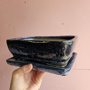 May include: A rectangular ceramic bonsai pot with a deep navy blue and black mottled glaze finish. The pot features a matching rectangular drip tray underneath, both showcasing a glossy, reflective surface with subtle variations in colour.