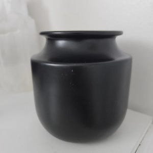 Peut inclure: Un vase en céramique noir mat avec un corps arrondi et un bord légèrement évasé. Le vase a un design lisse et minimaliste, adapté pour exposer des fleurs ou comme élément décoratif. Le vase est posé sur une surface blanche.