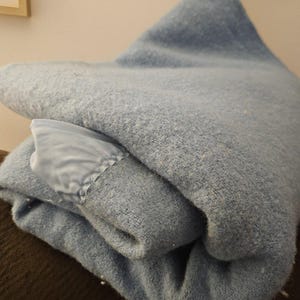 May include: A folded blue blanket with a satin trim. The blanket is made of a soft, fuzzy material.