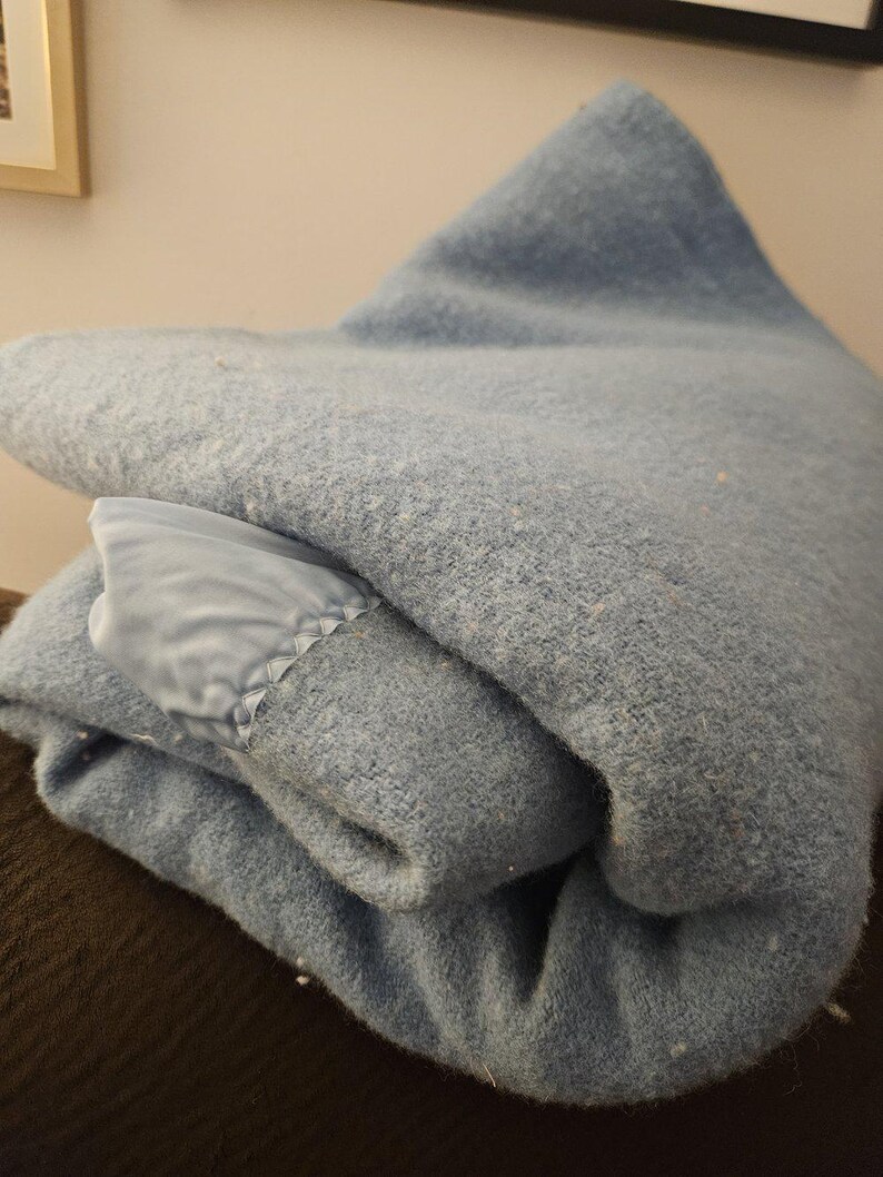 May include: A folded blue blanket with a satin trim. The blanket is made of a soft, fuzzy material.