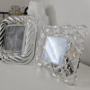 Puede incluir: Dos marcos de fotos de cristal transparente, uno con un diseño de espiral y el otro con un diseño geométrico.