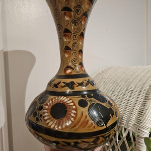 May include: A brown ceramic vase with black and orange painted designs. The vase has a wide base and a narrow neck.