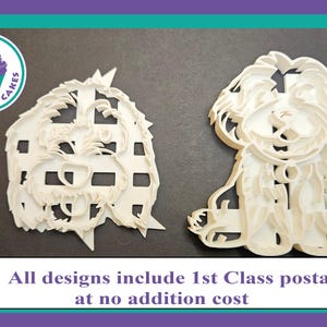 May include: Two white plastic cookie cutters shaped like dogs. One cutter is a side profile of a dog with its tongue sticking out. The other cutter is a front-facing dog with its tongue sticking out. The cutters are on a grey surface.