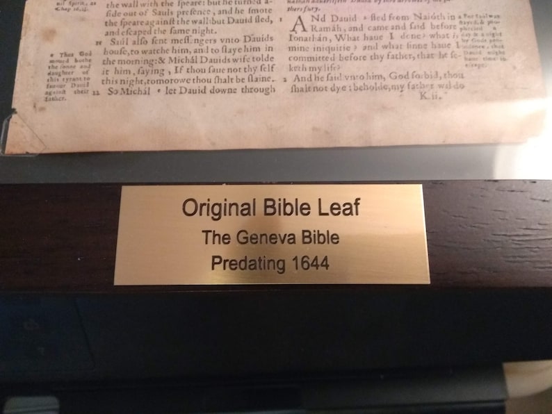 Puede incluir: Una placa dorada con texto negro que dice "Original Bible Leaf, The Geneva Bible, Predating 1644".