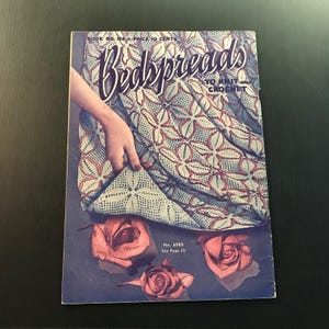 May include: Vintage "Bedspreads to Knit and Crochet" book cover. The cover features a hand holding up a section of a patterned bedspread. The cover is blue with the title in cursive and images of roses.