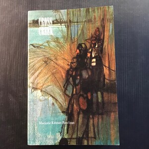 May include: A paperback book titled "Cross Creek" by Marjorie Kinnan Rawlings. The cover features an illustration of a waterside scene with figures and foliage in shades of blue, green, and brown. The title is in white letters.