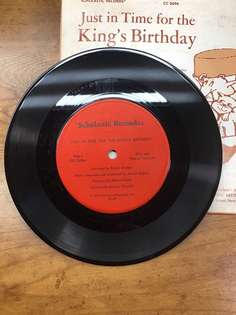 Peut inclure: Un disque vinyle noir avec une &eacute;tiquette rouge. L'&eacute;tiquette indique "Scholastic Records" et "Just in Time for the King's Birthday". Le disque tourne &agrave; 33 1/3 tours par minute et a une dur&eacute;e de lecture de 6:55.