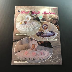 May include: A vintage crochet pattern book titled "Bed Doll Babies" by Annie Potter. The cover features three doll designs: "Easter Parade," "Granny's Darlin'," and "Little Sweetheart." Each doll is dressed in a crocheted dress and bonnet.