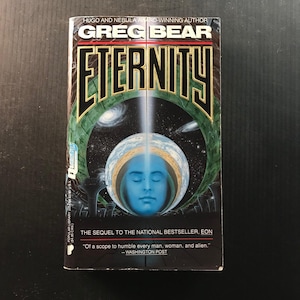 May include: A paperback book titled "Eternity" by Greg Bear. The cover features a blue face inside a globe, with a cosmic background. The book is a sequel to "Eon" and includes a quote from the Washington Post.