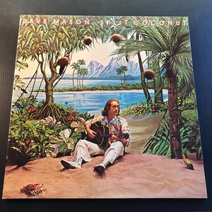 May include: Album cover for "Split Coconut" by Dave Mason. The artwork depicts a tropical scene with a man playing a guitar on a beach, surrounded by lush vegetation, coconuts, and a serene ocean view. The album title is visible at the top.