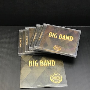 May include: A collection of Big Band music CDs. The cases are clear with gold lettering and a diamond pattern. The album art features the text "BIG BAND" and the "VAULTS" logo. Volumes 1, 2, 3, and 4 are visible.