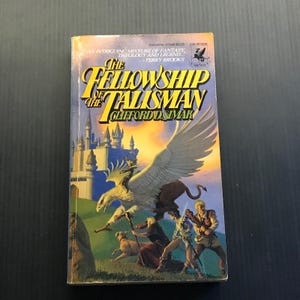 May include: A paperback book titled "The Fellowship of the Talisman" by Clifford D. Simak. The cover art features a griffin, figures in action, and a castle against a sunset sky. The book is a fantasy novel.