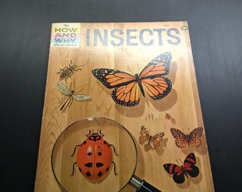May include: A vintage book titled "The How and Why Wonder Book of Insects" with illustrations of various insects. The cover features a ladybug magnified by a magnifying glass, a monarch butterfly, and other insects on a wood-grain background.