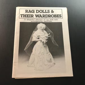 May include: A black and white image of a book titled "RAG DOLLS & THEIR WARDROBES". The book cover features a photograph of a rag doll in a wedding dress and veil. The text "A delightful selection of rag dolls with accompanying wardrobes" is also visible.