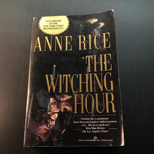 May include: A hardcover book titled "The Witching Hour" by Anne Rice. The cover is predominantly black with gold lettering and features an illustration of figures and candles. The book is labeled as a New York Times bestseller.