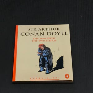 May include: A paperback book titled "The Man with the Twisted Lip" by Sir Arthur Conan Doyle. The cover features an illustration of a man in a blue coat. The book is part of the Penguin 60s series.