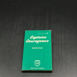 May include: A vintage paperback book titled "Captains Courageous" by Rudyard Kipling. The book has a green cover with white lettering and the "AB" Best Seller Classics logo. The book is a classic novel.