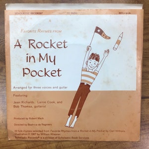 Peut inclure: Une pochette d'album de disque vinyle vintage avec une illustration de dessin anim&eacute; d'un gar&ccedil;on tenant une fus&eacute;e et un drapeau. Le titre de l'album est "A Rocket in My Pocket" et comporte le texte "Favorite Rhymes From".