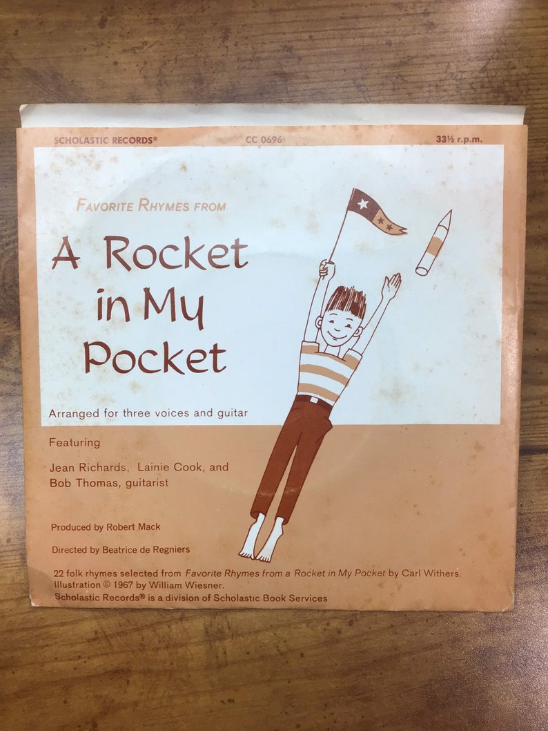 Peut inclure: Une pochette d'album de disque vinyle vintage avec une illustration de dessin anim&eacute; d'un gar&ccedil;on tenant une fus&eacute;e et un drapeau. Le titre de l'album est "A Rocket in My Pocket" et comporte le texte "Favorite Rhymes From".