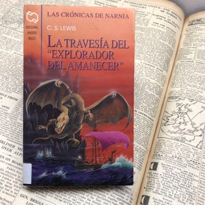 May include: A red, orange, and yellow book cover with a dragon illustration. The book title is "La Travesía del "Explorador del Amanecer" and the author is C.S. Lewis. The book is part of the "Las Crónicas de Narnia" series.