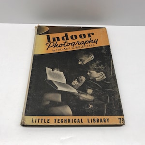 May include: Vintage book titled "Indoor Photography" by Hillary G. Bailey, F.R.P.S. The cover features a sepia-toned image of two people reading a book. The book is part of the "Little Technical Library" series, with the number 79 visible.