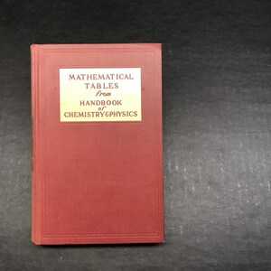 May include: A red hardcover book titled "MATHEMATICAL TABLES from HANDBOOK of CHEMISTRY & PHYSICS" with a white rectangular label. The book has a textured cover and is likely a reference book for scientific calculations.