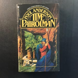 May include: A vintage paperback book titled "Time Patrolman" by Poul Anderson. The cover features a warrior in blue cloak and hat, holding a spear in a forest setting. The title is in gold lettering.