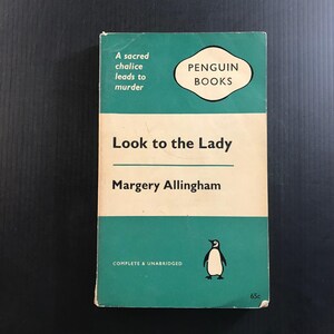 May include: A vintage Penguin Books paperback titled Look to the Lady by Margery Allingham. The cover features a teal and cream color scheme with the text A sacred chalice leads to murder, the Penguin Books logo, and a small penguin illustration.