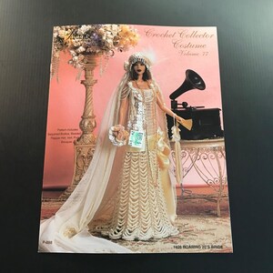 May include: A vintage crochet pattern book titled "Crochet Collector Costume Volume 77." The cover features a doll in a cream-colored crochet wedding dress with a veil and beaded accents. The background is pink with a vintage gramophone.