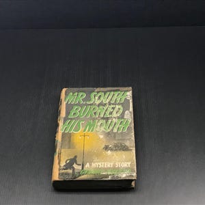 May include: A vintage book titled "Mr. South Burned His Mouth" with a mystery story theme. The cover features a silhouette of a person running, a car, and a yellow sun. The book has a worn appearance.